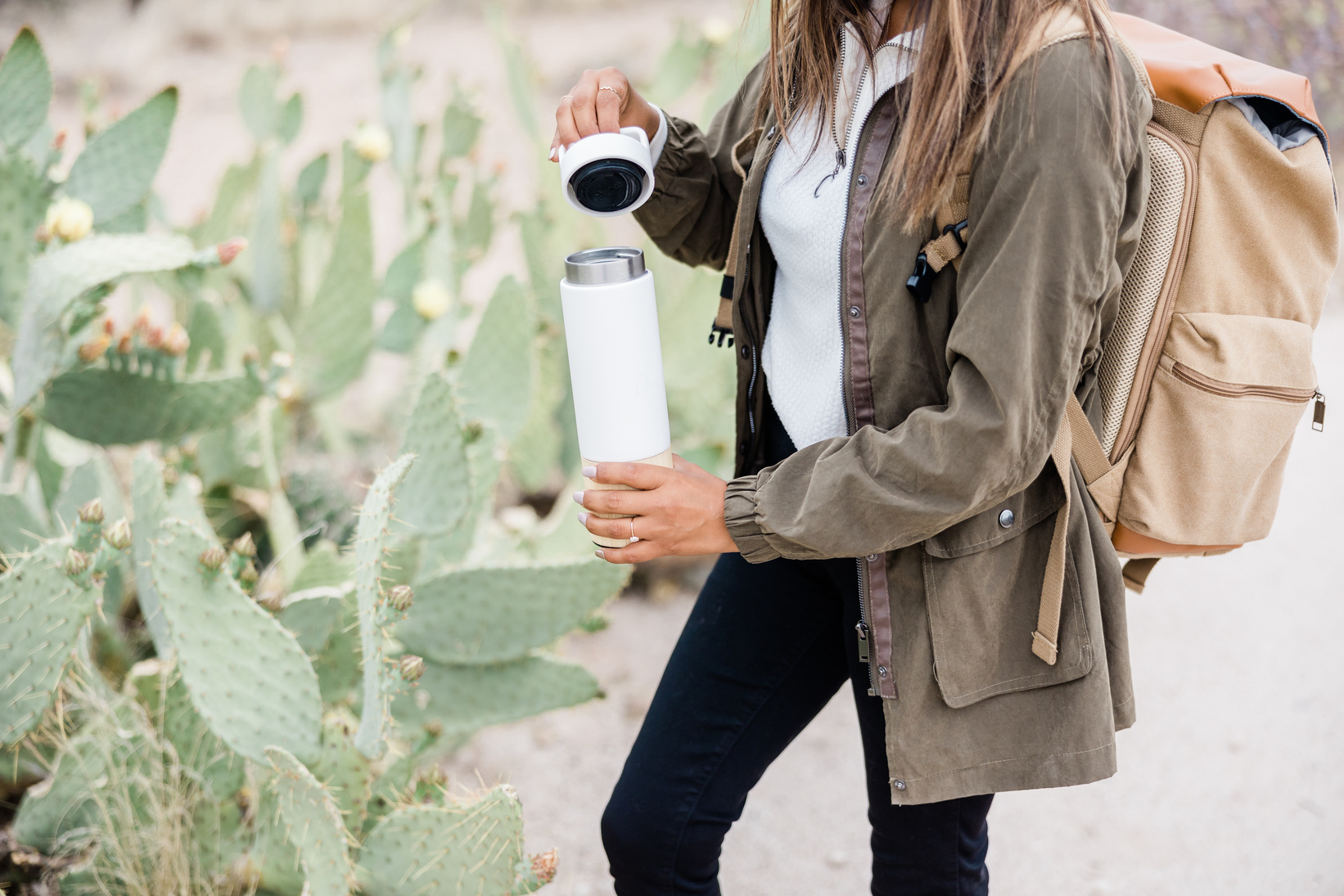 Woman with Backpack Holding Water Tumbler in a Desert